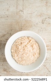 A White Bowl Of Porridge Oats Or Oatmeal On A Natural Wooden Background. Shot Overhead With Space For Copy Or Text