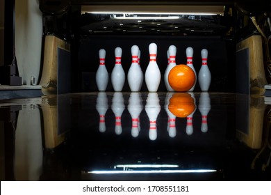 White Bowling Pins And An Orange Ball On A Bowling Alley. Beautiful Reflection. Close-up. Front View.