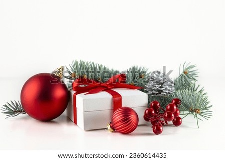 A white box with a gift tied with a red ribbon, a spruce branch and obligatory decorations on a white background.