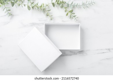 White Box Open On Marble Table With Green Plant, Flatlay