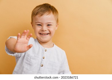 White Boy With Down Syndrome Smiling And Gesturing At Camera Isolated Over Beige Background