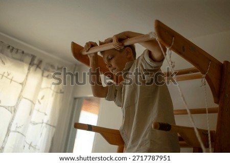 white boy practicing hanging exercises on wooden bars, determined face shows early gymnastic training and strength building