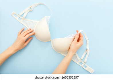 White Bra in female hands. Woman choosing holding white bra lingerie on blue background. Flat lay with lace underwear bra. Beautiful sexy full coverage bra. Sale, special offer, lingerie store concept