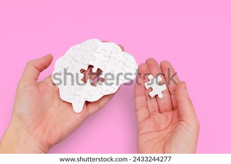 White brain-shaped jigsaw puzzle in one hand and the missing puzzle piece in the other. Journey to mental health and well-being.