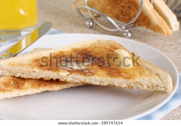 White bread toast with melting butter in\
a breakfast setting with juice and a toast\
rack