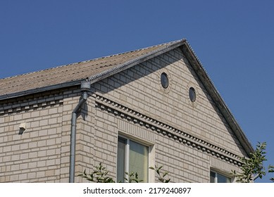 White Brick Attic Of A Private House With A Window Under A Gray Slate Roof Against The Blue Sky