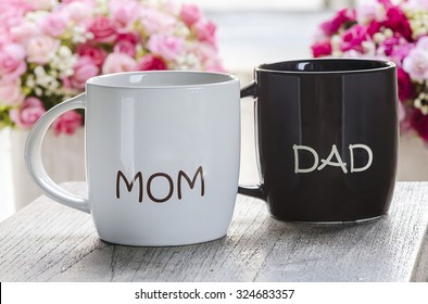 White And Brown Ceramic Mug With Print Word Mom And Dad On Wooden Background,soft Focus.