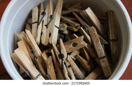 A White Bucket Filled With Old Wooden Pegs Or Clothespin.