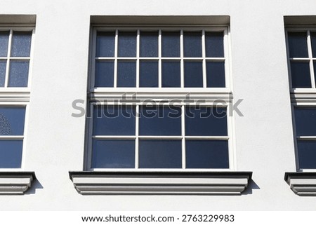 White building facade with classic window frames and clean geometry. Architectural detail of residential house exterior. Symmetry and minimal design in urban environment.