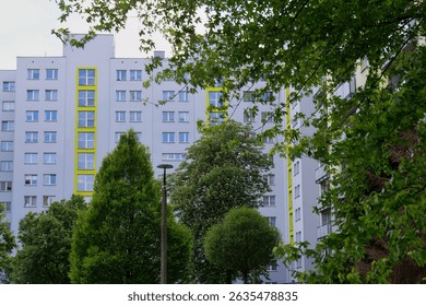 A white building with yellow window frames is partially hidden by trees in Sosnowiec - Silesia - Poland