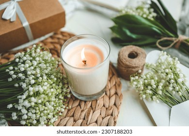 A white burning candle and a bouquet of lilies of the valley, a natural spring photo. - Shutterstock ID 2307188203