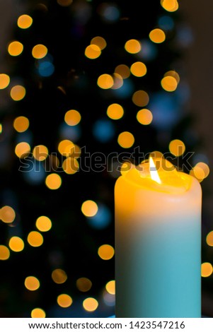 White burning candle with a dark background with outof focus colored lights of a christmastree