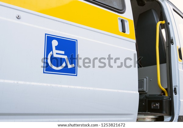 White bus with a blue sign for the disabled.\
The open door of a specialized vehicle for people with\
disabilities. Yellow bar and\
handrail.
