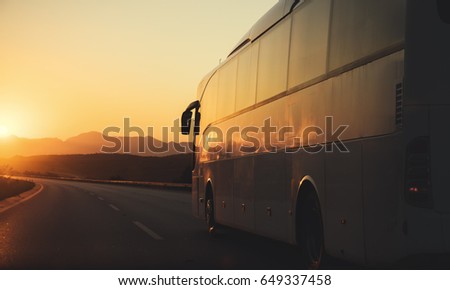 White bus driving on road towards the setting sun