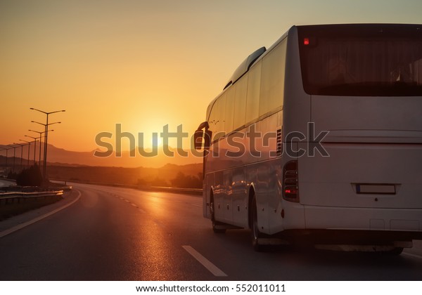 White bus\
driving on road towards the setting\
sun