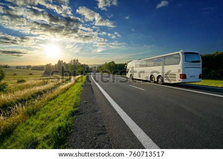 White bus traveling on the asphalt road in a rural landscape at sunset