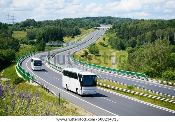 White buses driving on the highway winding\
through forested areas. View from\
above.