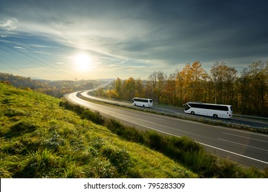 White buses traveling on the highway turning towards the horizon in an autumn landscape at sunset
