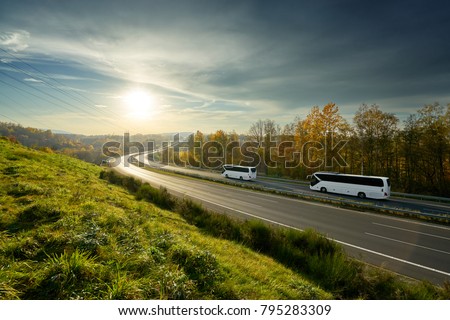 White buses traveling on the highway turning towards the horizon in an autumn landscape at sunset