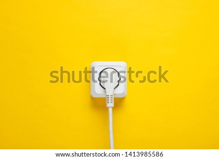 White cable plugged into power outlet on yellow wall background