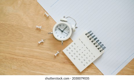 white calendar, thumbtack and analog alarm clock on school paper with line on wooden desk for back to school concept