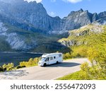 White camper van driving on a scenic road amidst mountains in norway, offering a picturesque view of travel and adventure