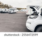 White camper van with open hood parked in a dealership parking lot surrounded by other recreational vehicles