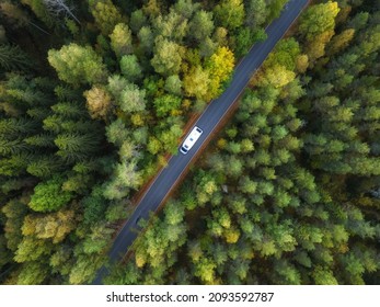 White camper van with solar panels drive through green forest. Aerial top down view. Travel concept.

