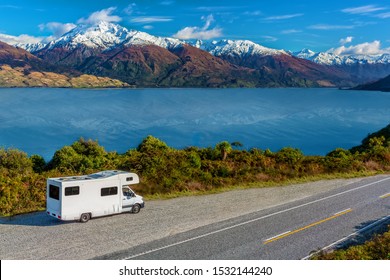 A white camper-van / RV parked in a lay-by viewpoint on the banks of Lake Wanaka with the lake and the dramatic snow capped peaks in the distance.