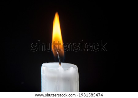 A white candle with burning candle flame on a black background, close up, isolated