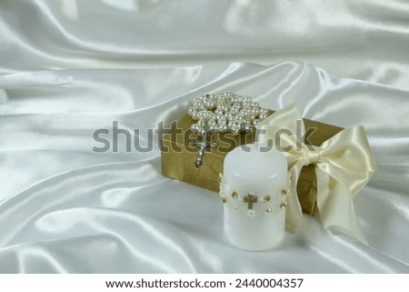 White candle, rosary and gift box on white background. Baptism concept.