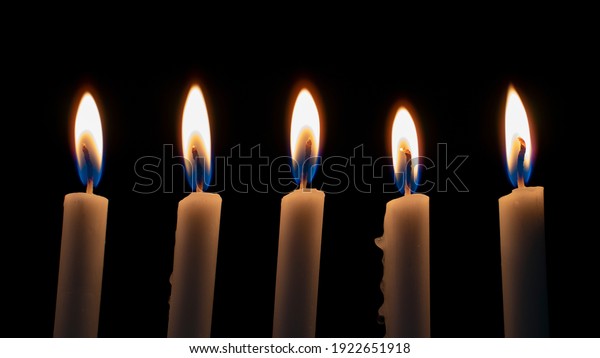 White Candles Burning in the Dark with lights\
glow. The burning candle\'s flame in the dark background. a symbol\
of the Christian faith. Candles Burning in the Dark with lights\
glow.White Candles