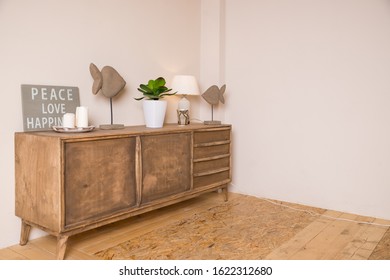 A White Candles, Lamp And A Small Potted Plant Are Placed On The Chest In The Living Room.Candles, Decor And Green Plant In White Pot On The Table In Elegant Stylish Apartment.home Decor. Interior