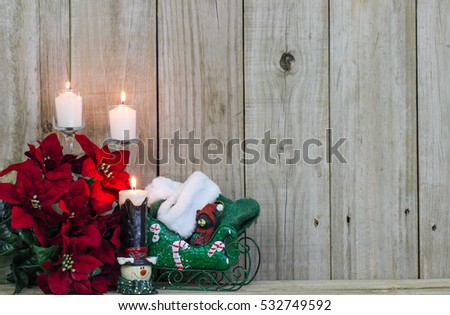 White candles, red poinsettias, snowman and green Christmas sleigh by rustic antique wooden background; holiday background with Christmas decorations and wood copy space