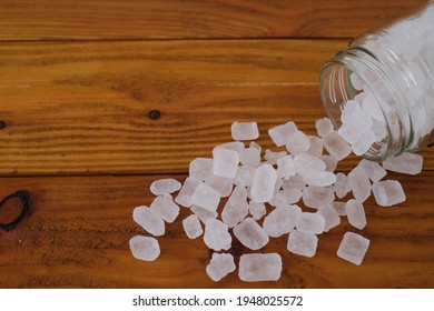 White Candy Rock Sugar Or Crystal Sugar In Glass Jar Isolated On Wooden Background. White Rock Sugar Is Melted And Then Allowed To Crystallize Into Semi-translucent Gemstone.