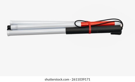 White cane for visually impaired person, folded and held together with red elastic band, lying on white background