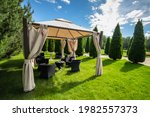 White canvas gazebo with plastic garden furniture in a summer green lawn.