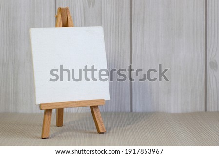 White canvas on a small easel on a light wooden background, close up, blank sheet concept with copy space