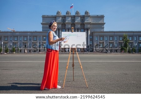 White canvas on a wooden tripod. A woman artist paints a city landscape.