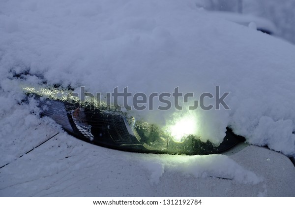 White car covered with snow and the headlights\
turned on in light green