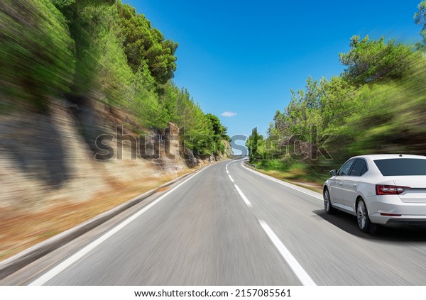 A white car drives along a beautiful road on a sunny\
summer day.