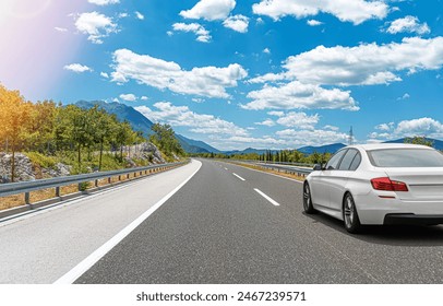 A white car drives along the highway against the backdrop of rocky mountains on a sunny day. - Powered by Shutterstock