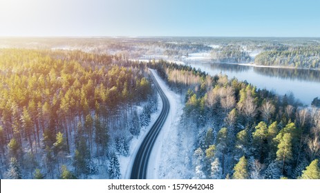 White car drives empty road running along the beautiful blue lake in the cold Finnish winter. Tourists on road trip cruising through the idyllic snow covered countryside and woods. - Powered by Shutterstock