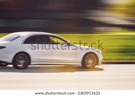 A white car is driving down the street at high speed. Large luxury sedan with motion blur background. Abstract photography of a fast moving blurred car on a speed blurred background.