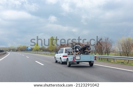 White car driving on highway with trailer holding motorcycle 