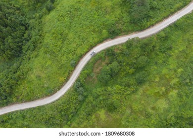 A White Car Driving On A Winding Road In The Lush Mountainous Area