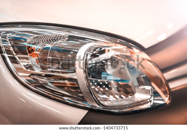 White car front light. The reflector is\
corrugated. Visible parts of the inner part of the headlight. The\
background is blurred.