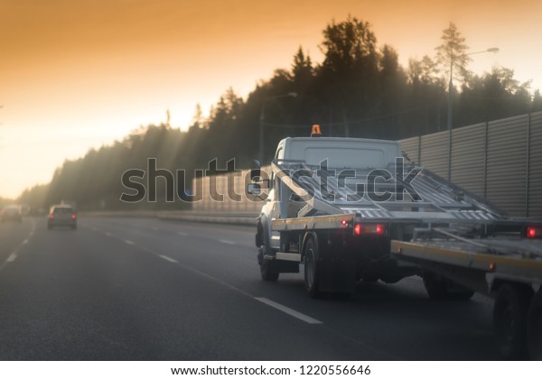 A white car\
hauler truck with an empty two-tiered trailer for transporting cars\
is moving along the broadband scenic highway. road with metal\
safety and sound barrier