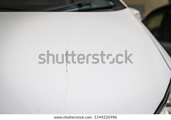 The white car hood has scratches. Until rusting on\
the car\'s steel plate
