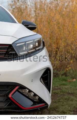 white car with LED headlights against a background of yellowed autumn trees